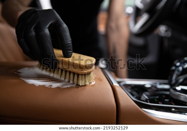 car detailing studio employee cleans the brown\
leather upholstery of a car\
