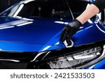 Car detailing studio or car wash worker applying ceramic car coating on blue car hood