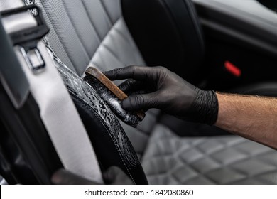 Car detailing studio worker cleaning car interior and car leather seats with a brush.