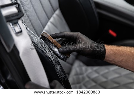 Car detailing studio worker cleaning car interior and car leather seats with a brush.