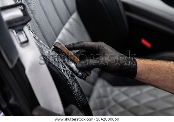 Car detailing studio worker cleaning car\
interior and car leather seats with a\
brush.