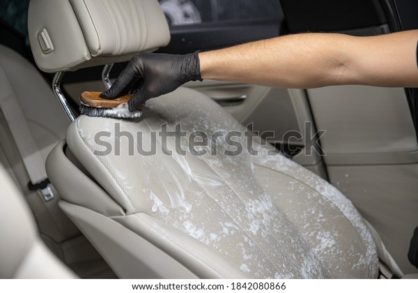 Car detailing studio worker cleaning car\
interior and car leather seats with a\
brush.