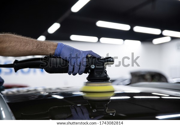 Car detailing studio. Worker polishing\
scratched car paint with electric\
polisher.