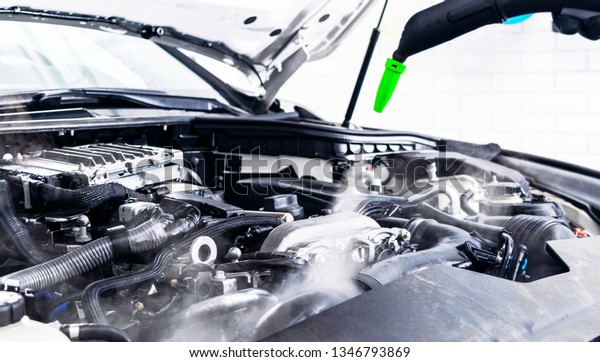 Car detailing. Car washing cleaning\
engine. Cleaning car using hot steam. Hot Steam engine washing.\
Soft lighting. Car wash man worker cleaning\
vehicle.