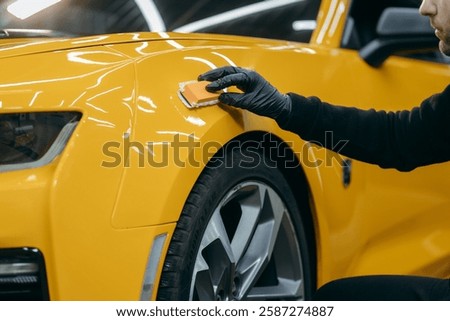 Car detailing worker applying ceramic car coating on yellow car at workshop