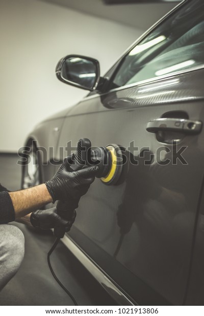 Car detailing - Worker with orbital\
polisher in auto repair shop.  Selective\
focus.