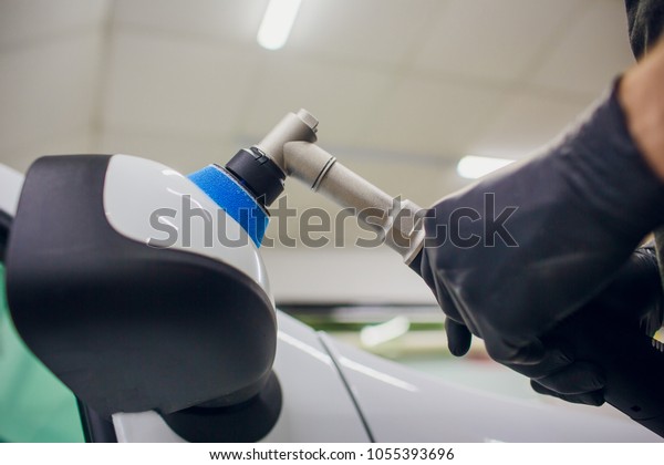 Car detailing - Worker\
with orbital polisher in auto repair shop. Car mirror polish.\
Selective focus.