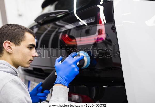 Car detailing - Worker with orbital\
polisher in auto repair shop. Selective\
focus.