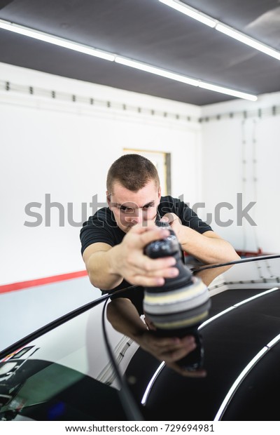 Car detailing - Worker with orbital\
polisher in auto repair shop. Selective focus.\
