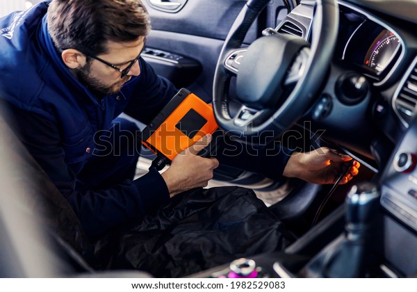 Car\
diagnostics at technical inspection, car electronics. A man in a\
blue uniform holds a digitizing device and checks the condition of\
the string inside the car under the steering\
wheel