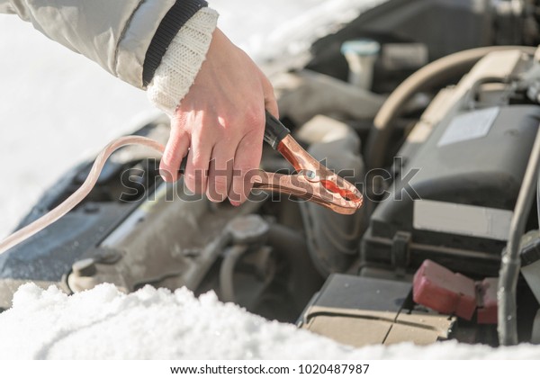The car did not start because of the cold\
temperature. The woman connects the terminals to the battery. Day,\
winter, frost.