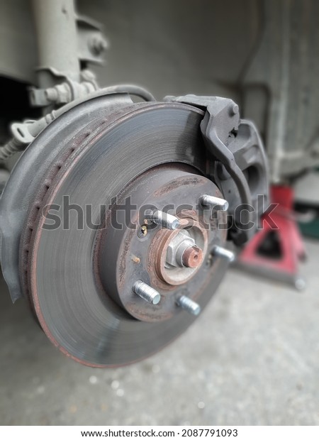 Car disc with its disc brakes that produce a\
friction to resist rotation of the circular plate within the wheel,\
car is elevated with hydraulic trolley jack and a supportive stand\
for tyre replacement