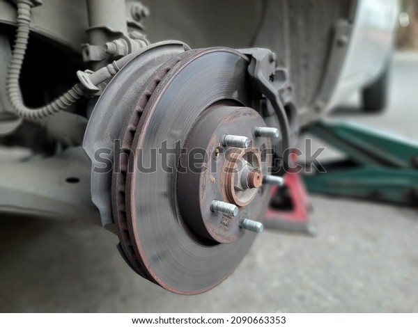 Car disc with its disc brakes that produce a\
friction to resist rotation of the circular plate within the wheel,\
car is elevated with hydraulic trolley jack and a supportive stand\
for tyre replacement