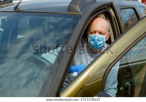 Car disinfection. A man in\
gloves and a mask wipes the steering wheel with a disinfectant\
wipe.