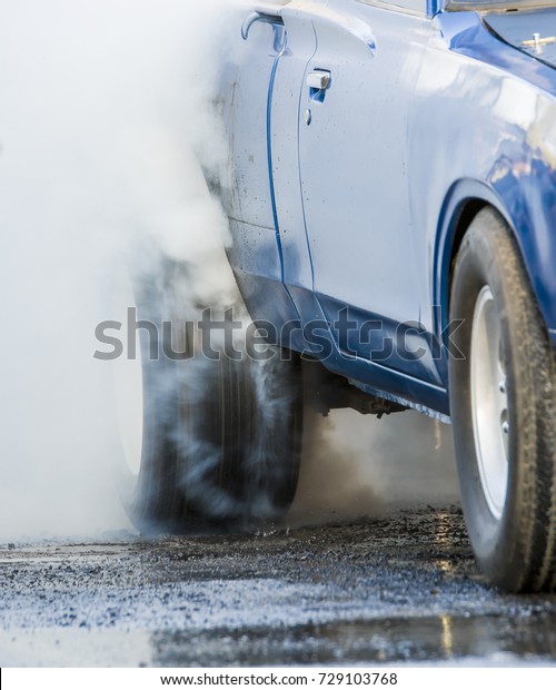 Car doing\
a burnout. The rear tire is spinning very fast and making much\
smoke. Car is blue but not identifiable.\
