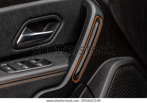 Car door handle with power window control. Dark\
leather interior of modern car. Dark black and orange car leather\
pleats stitch. Details of door handle with windows controls. Car\
window controls.