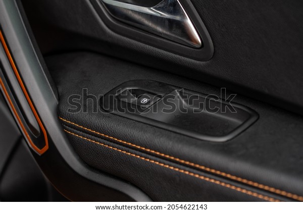 Car door handle with power window control. Dark\
leather interior of modern car. Dark black and orange car leather\
pleats stitch. Details of door handle with windows controls. Car\
window controls.