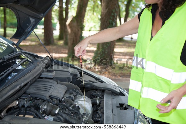 Car is down and a woman check the oil level with her\
yellow vest