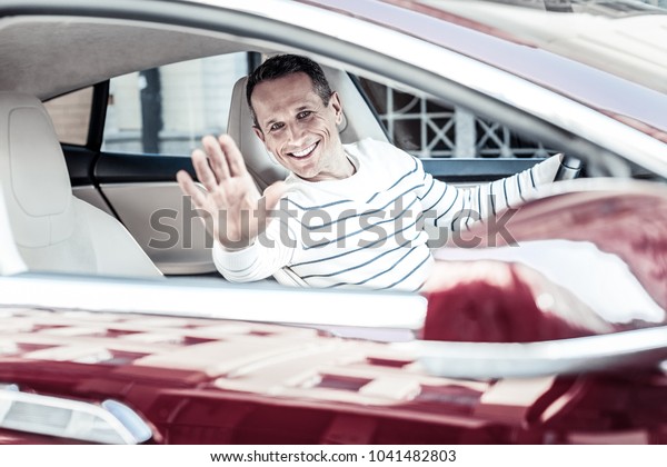 Car driver. Happy\
positive nice man sitting behind the wheel and waving his hand\
while greeting a friend