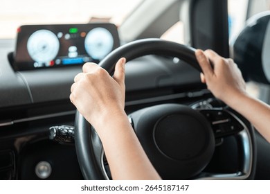 A car driver is holding and controlling on steering wheel of the modern car with digital display as background, close-up and selective focus a person hand. Transportation with people in action scene.