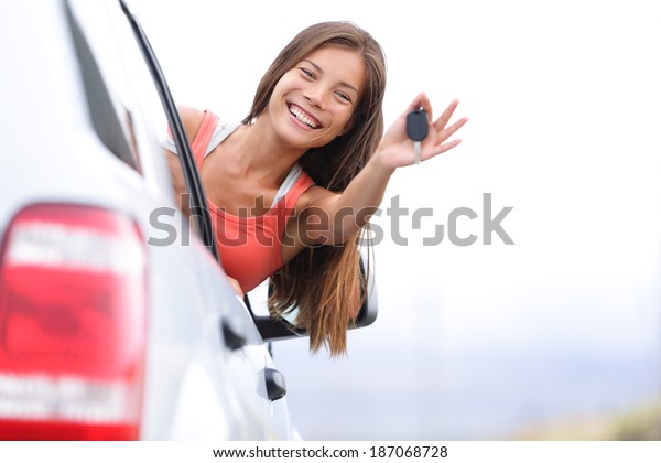 Car driver woman\
happy showing car keys out window. New car, rental or driving\
licence concept with young female model on road trip. Mixed race\
Asian Caucasian girl in her\
20s.