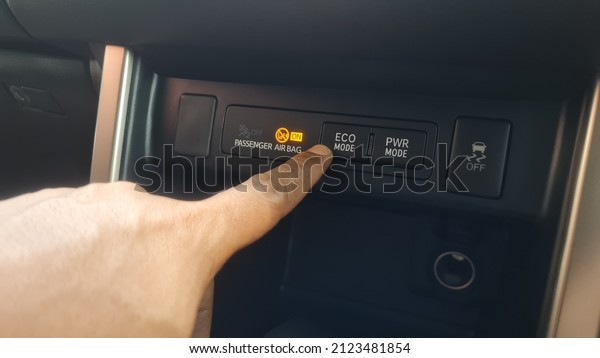 The car driver\'s finger\
presses the eco mode button on a car to make a car\'s fuel\
consumption economical