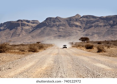 A Car Drives Along A Dirt Or Gravel Road In The Dry, Arid, Rural Landscape Of Namibia.