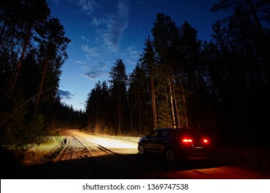 The car drives along a dirt road in the woods against the background of the night sky, brightly lit headlights. Romantic travel and adventure, Rear view