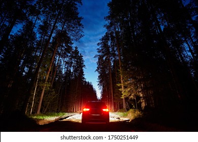 The car drives along a dirt road in the woods against the background of the night sky, brightly lit headlights. Romantic travel and adventure, Rear view