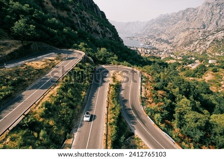 Car drives along a serpentine highway in the mountains overlooking the Bay of Kotor. Montenegro. Drone