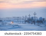 The car drives along a snow-covered road past large satellite dishes. Industrial arctic landscape. Cold frosty and windy winter weather. Chukotka, Siberia, Far North of Russia.