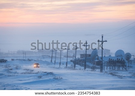 The car drives along a snow-covered road past large satellite dishes. Industrial arctic landscape. Cold frosty and windy winter weather. Chukotka, Siberia, Far North of Russia.