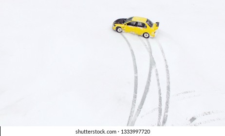 Car Drives By Icy Track On Snow Covered Lake At Winter. Aerial View. Sport Car Racing On Snow Race Track In Winter. Driving A Race Car On A Snowy Road