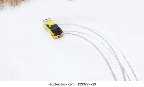 Car Drives By Icy Track On Snow Covered Lake At Winter. Aerial View. Sport Car Racing On Snow Race Track In Winter. Driving A Race Car On A Snowy Road