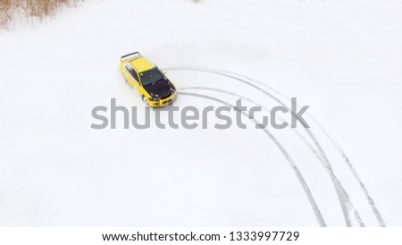 Car drives by icy track on snow covered lake at winter. Aerial view. Sport car racing on snow race track in winter. Driving a race car on a snowy road