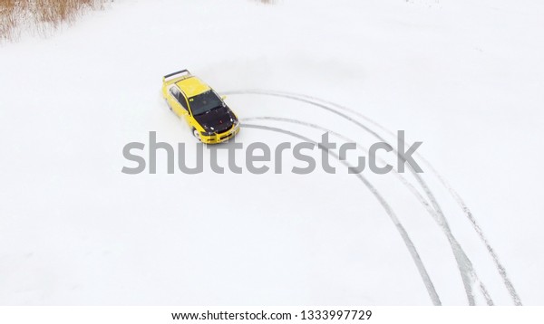 Car drives by icy track on snow covered\
lake at winter. Aerial view. Sport car racing on snow race track in\
winter. Driving a race car on a snowy\
road
