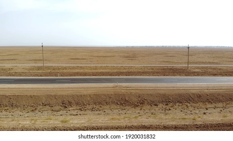 A Car Drives By On An Empty Road. The Drone Follows The Car On A Narrow Asphalt Road. The Car Drives Through The Desert. Side View Of A Passing Car