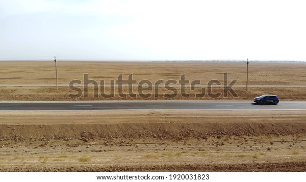 a car drives by on an empty road. The\
drone follows the car on a narrow asphalt road. the car drives\
through the desert. side view of a passing\
car
