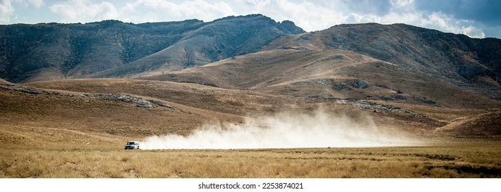 The car drives quickly through the mud with clouds of dust from under the wheels, against the backdrop of the mountains. Rally Dakar. Off-road vehicle rides off-road in the desert. - Powered by Shutterstock