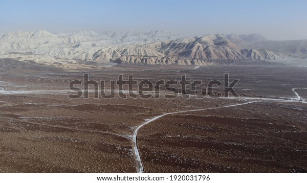 the car drives through the desert into the\
distance. Taken from a drone.\
The car drives through the desert\
landscape.\
Aerial shot of car driving through snow on isolated\
dirt road in desert\
landscape