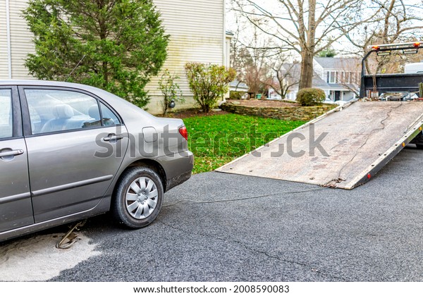 Car in driveway with tow truck for vehicle due to\
fuel leak that damaged pavement covered in cat litter to absorb the\
gas