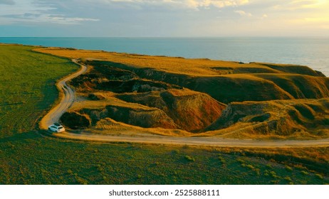 Car driving along a coastal road with cliffside views at sunset. A car drives along a coastal dirt road, surrounded by grassy cliffs and the sea in the distance. - Powered by Shutterstock