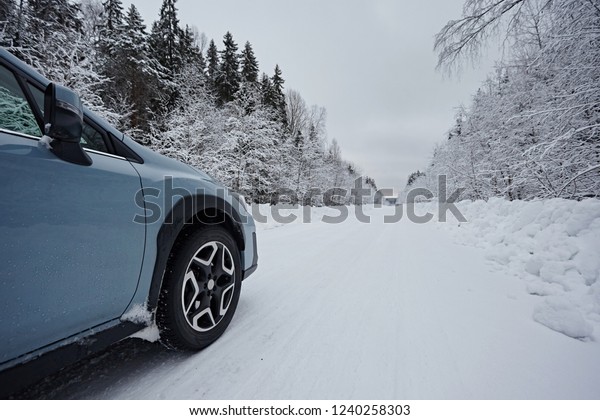 A
car  is driving along a winter road amid a snowy forest after a
snowfall in cloudy weather. Driving in the dangerous conditions of
the north. Close-up to the front and wheel with
tire