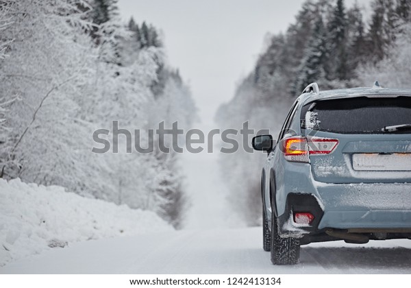 A car is driving along a\
winter road amid a snowy forest after a snowfall in cloudy weather.\
Driving in the dangerous conditions of the north. Bumper rear\
view