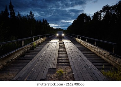 The car is driving along the wooden road of the bridge from planks against the background of the night sky in the forest, its headlights are bright - Powered by Shutterstock
