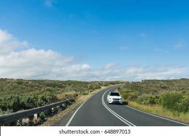 Car Driving Down Curved Coastal Road On Sunny Day