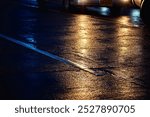 A car is driving down a wet road at night. The reflection of the car is visible in the wet pavement