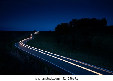 Car Driving Down A Winding Country Road, Long Exposure, Head Lights In Blurred Motion