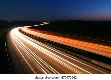 Car Driving Down A Winding Motorway At Night, Long Exposure Of Headlights And Taillights In Blurred Motion