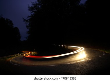 Car Driving Down A Winding Road At Night, Long Exposure Of Headlights An Taillights In Blurred Motion